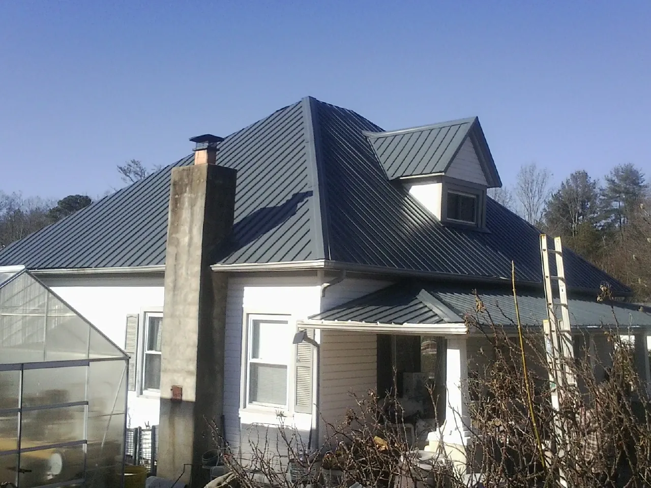Dark blue standing seam metal roof on a white farmhouse with dormer — Slate & Tile Roof Repair by Roofing Brothers in Aston