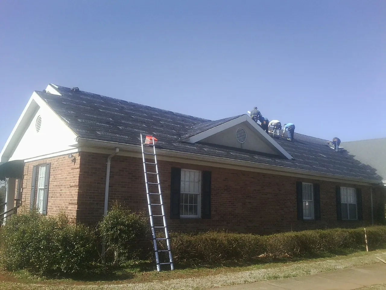 Crew tearing shingles off a brick ranch roof with a ladder set — Emergency Roof Repair work by our crew in Aston