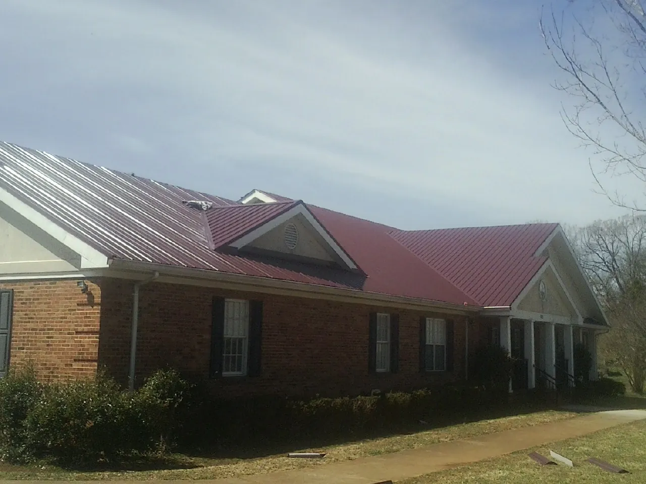 Red metal roof with gabled entries on a long brick building, from a Hail Damage Roof Repair job in Aston