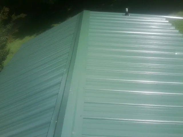 New green metal panels meeting at the ridge of a roof — Flat Roof Repair work by our crew in Aston