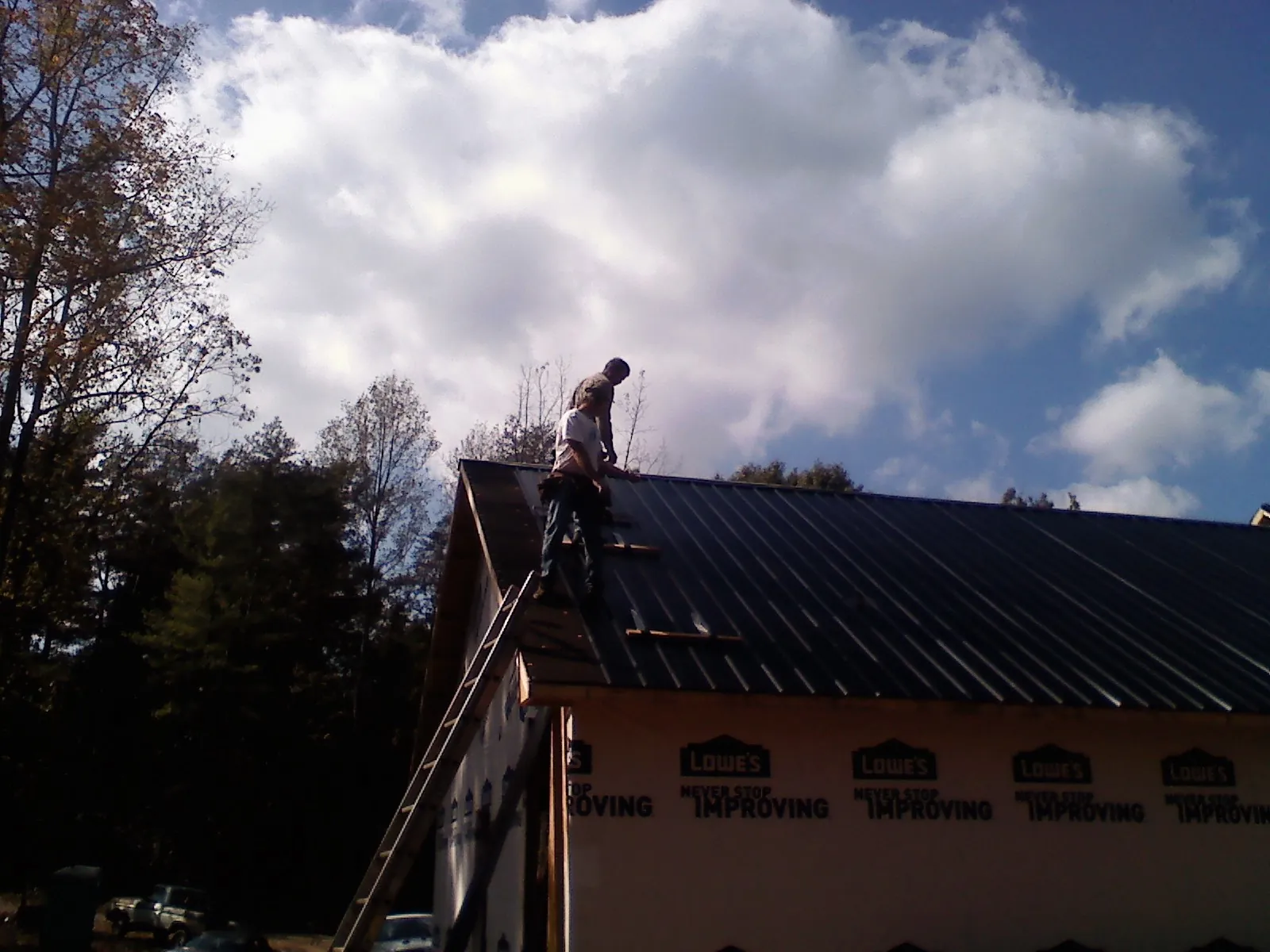 Roofer fastening dark metal panels high against a cloudy sky, from a Roof Inspection job in Aston