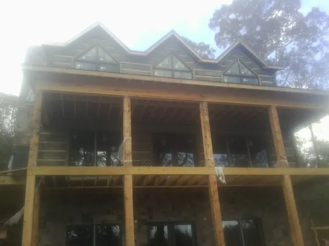 Dormers and porch framing on a large log home under construction — Roof Coating work by our crew in Aston