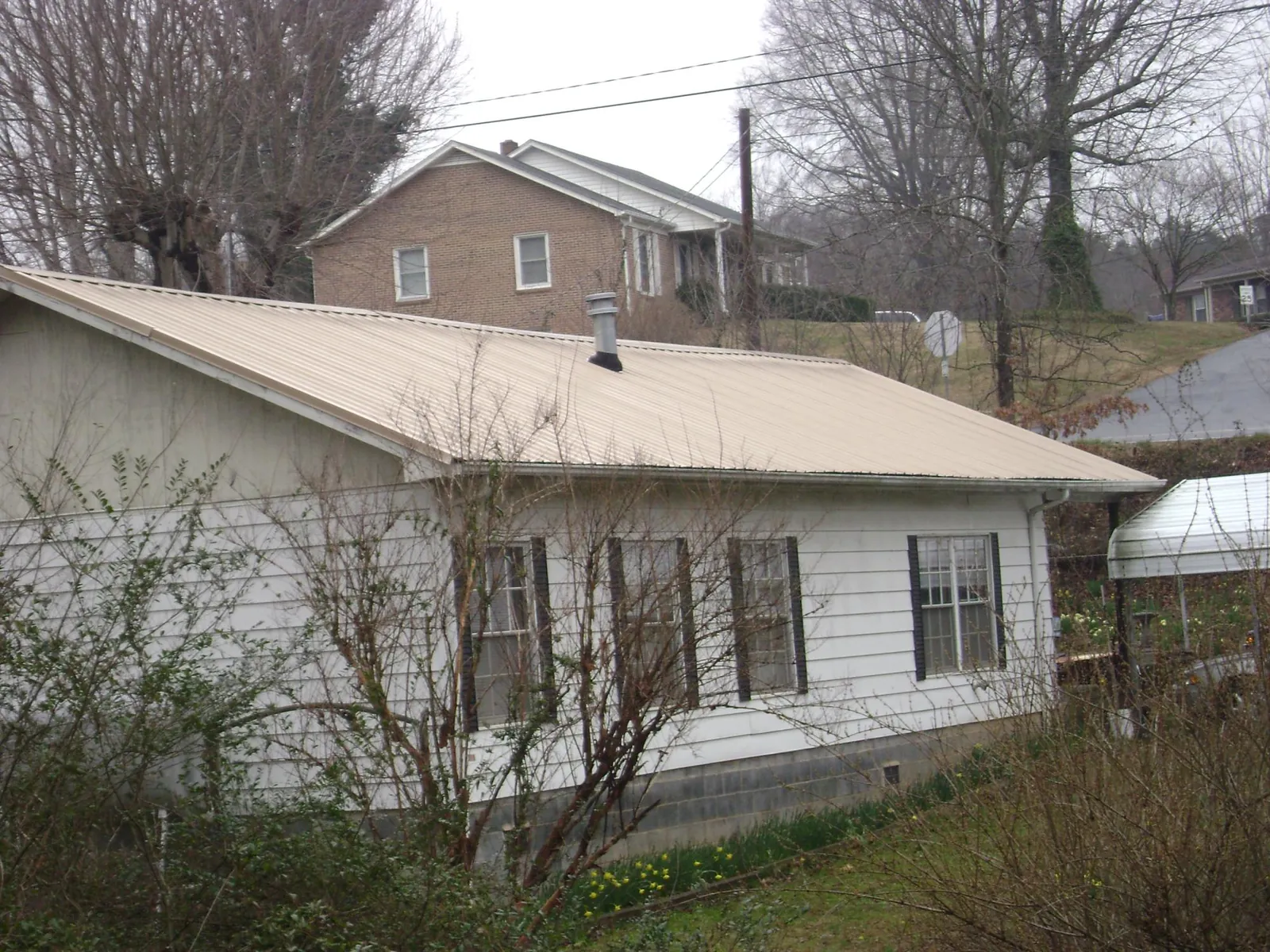 Tan metal roof on a white sided house set into a hillside — Commercial Roofing by Roofing Brothers in Aston